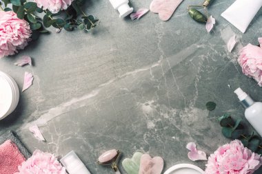 Yüz silindiri, gua sha masaj aleti, yağ şişesi, havlu, mermer arka planda pembe şakayıklar. Uzayı kopyala Düz yatıyordu. Üst Manzara. Rutin cilt bakımı, vücut bakımı, spa konsepti