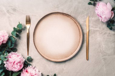 Sofra takımı, şenlik masasına servis edilen çiçekler, akşam yemeği. Taş kaplama tabaklar, altın çatal bıçak takımı, okaliptüs dalları, mermer arka planda şakayık çiçekleri. Uzayı kopyala Düz yerde, üst tarafta. Tablo ayarı.