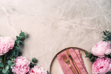 Sofra takımı, şenlik masasına servis edilen çiçekler, akşam yemeği. Taş kaplama tabaklar, altın çatal bıçak takımı, okaliptüs dalları, mermer arka planda şakayık çiçekleri. Uzayı kopyala Düz yerde, üst tarafta. Tablo ayarı.