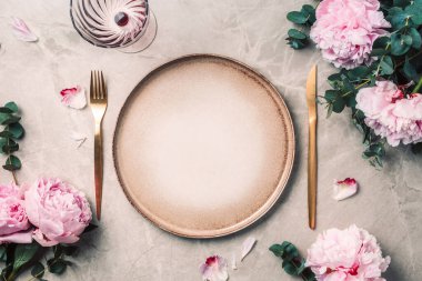 Sofra takımı, şenlik masasına servis edilen çiçekler, akşam yemeği. Taş kaplama tabaklar, altın çatal bıçak takımı, okaliptüs dalları, mermer arka planda şakayık çiçekleri. Uzayı kopyala Düz yerde, üst tarafta. Tablo ayarı.