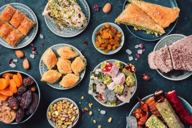 Karanlık arka planda Orta Doğu tatlıları. Arap tatlısı, baklava, halva, rahat lokum, şerbet, fındık, şam fıstığı, hurma, kuru üzüm, kayısı, kilise kilisesi, kurabiye. Üst Manzara. Düz yatıyordu. Boşluğu kopyala.