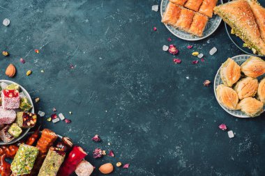 Karanlık arka planda Orta Doğu tatlıları. Arap tatlısı, baklava, halva, rahat lokum, şerbet, fındık, şam fıstığı, hurma, kuru üzüm, kayısı, kilise kilisesi, kurabiye. Üst Manzara. Düz yatıyordu. Boşluğu kopyala.