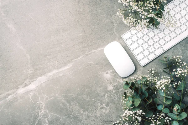 Feminine workspace. White computer keyboard, mouse, gypsophila flowers, eucalyptus flowers on marble background. Top view. Copy space. Flat lay. Blogger, business concept. Mock up. Birthday, Woman day