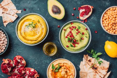 Sarı humus ve yeşil humus, tahini, zeytinyağı, susam tohumu, pita, çiğ nohut, avokado, koyu arkaplanda nar. Ortadoğu, Yahudi, Arap mutfağı. Üst görünüm.