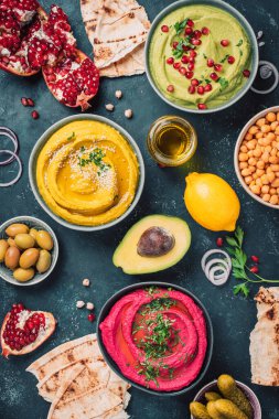 Sarı zerdeçal humusu, yeşil maydanoz humusu ve koyu arkaplanda kırmızı pancar humusu, limon, susam, zeytinyağı, pide, avokado, nar. Orta Doğu, Yahudi, Arap mutfağı