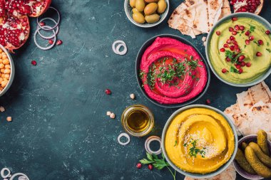 Sarı zerdeçal humusu, yeşil maydanoz humusu ve koyu arkaplanda kırmızı pancar humusu, limon, susam, zeytinyağı, pide, avokado, nar. Orta Doğu, Yahudi, Arap mutfağı