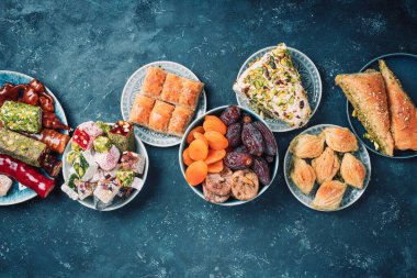 Karanlık arka planda Orta Doğu tatlıları. Arap tatlısı, baklava, halva, rahat lokum, şerbet, fındık, şam fıstığı, hurma, kuru üzüm, kayısı, kilise kilisesi, kurabiye. Üst Manzara. Düz yatıyordu. Boşluğu kopyala.