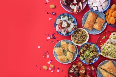 Kırmızı arka planda Orta Doğu tatlıları. Arap tatlısı, baklava, halva, rahat lokum, şerbet, fındık, şam fıstığı, hurma, kuru üzüm, kayısı, kilise kilisesi, kurabiye. Üst Manzara. Düz yatıyordu. Boşluğu kopyala.