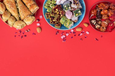 Kırmızı arka planda Orta Doğu tatlıları. Arap tatlısı, baklava, halva, rahat lokum, şerbet, fındık, şam fıstığı, hurma, kuru üzüm, kayısı, kilise kilisesi, kurabiye. Üst Manzara. Düz yatıyordu. Boşluğu kopyala.