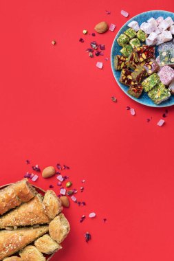 Kırmızı arka planda Orta Doğu tatlıları. Arap tatlısı, baklava, halva, rahat lokum, şerbet, fındık, şam fıstığı, hurma, kuru üzüm, kayısı, kilise kilisesi, kurabiye. Üst Manzara. Düz yatıyordu. Boşluğu kopyala.