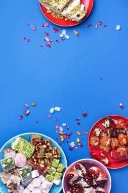 Mavi arka planda Orta Doğu tatlıları. Arap tatlısı, baklava, halva, rahat lokum, şerbet, fındık, şam fıstığı, hurma, kuru üzüm, kayısı, kilise kilisesi, kurabiye. Üst Manzara. Düz yatıyordu. Boşluğu kopyala.