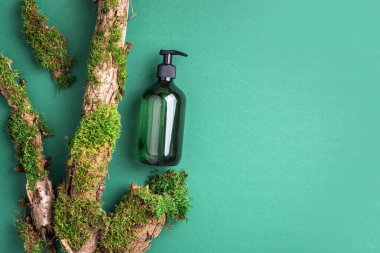 Yeşil arka planda etiketsiz kozmetik şişesi dalların üzerinde doğal yosun, ağaç kabuğu. Cilt bakımı, organik vücut bakımı, spa konsepti. Vegan çevre dostu kozmetoloji ürünü. Organik Kozmetik