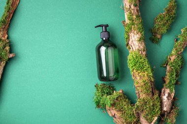 Yeşil arka planda etiketsiz kozmetik şişesi dalların üzerinde doğal yosun, ağaç kabuğu. Cilt bakımı, organik vücut bakımı, spa konsepti. Vegan çevre dostu kozmetoloji ürünü. Organik Kozmetik