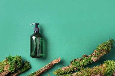 Yeşil arka planda etiketsiz kozmetik şişesi dalların üzerinde doğal yosun, ağaç kabuğu. Cilt bakımı, organik vücut bakımı, spa konsepti. Vegan çevre dostu kozmetoloji ürünü. Organik Kozmetik
