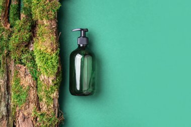 Yeşil arka planda etiketsiz kozmetik şişesi dalların üzerinde doğal yosun, ağaç kabuğu. Cilt bakımı, organik vücut bakımı, spa konsepti. Vegan çevre dostu kozmetoloji ürünü. Organik Kozmetik
