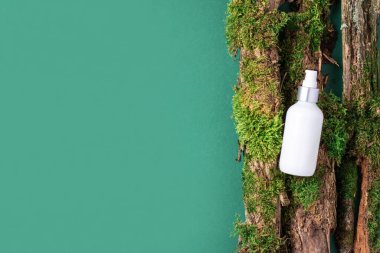 Yeşil arka planda beyaz etiketsiz kozmetik şişesi dalların üzerinde doğal yosun, ağaç kabuğu. Cilt bakımı, organik vücut bakımı, spa konsepti. Vegan çevre dostu kozmetoloji ürünü. Organik Kozmetik
