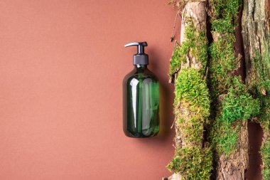 Yeşil cam şampuan, sabun, kahverengi arka planda saç kremi ve ağaç kabuğunun üstünde doğal yosun. Üst görünüm, boşluğu kopyala. Model için boş etiket. Cilt bakımı, organik vücut tedavisi, spa konsepti.