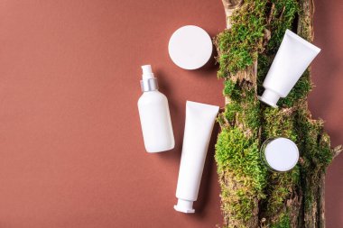 Krema kavanozu, nemlendirici losyon, şampuan ya da diğer kozmetik ürünler kahverengi arka planda beyaz boş şişede, yosun ve ağaç kabuğuyla. Cilt bakımı, organik vücut bakımı, spa konsepti. Vejetaryen çevre dostu.