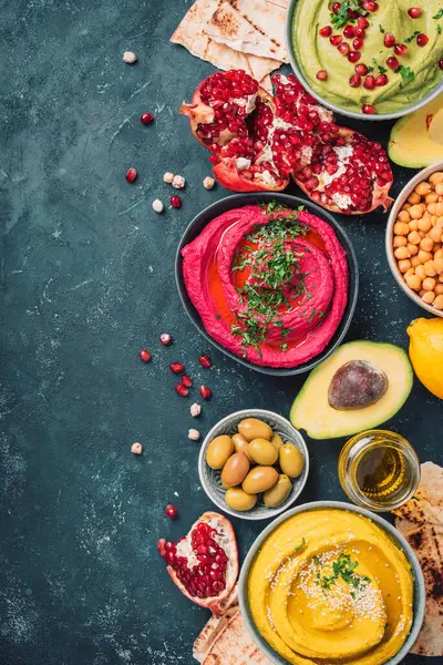 Renkli humus kaseleri. Koyu arka planda yeşil, sarı ve pancar humusu. Limon, zeytin yağı, susam tohumu, pita, çiğ nohut, avokado, nar. Orta Doğu, Yahudi, Arap mutfağı