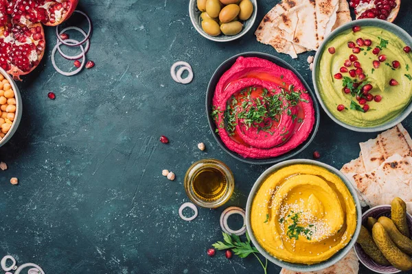 Sarı zerdeçal humusu, yeşil maydanoz humusu ve koyu arkaplanda kırmızı pancar humusu, limon, susam, zeytinyağı, pide, avokado, nar. Orta Doğu, Yahudi, Arap mutfağı