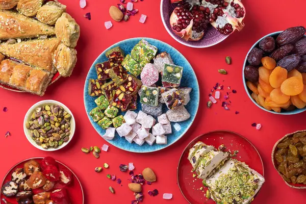 Kırmızı arka planda Orta Doğu tatlıları. Arap tatlısı, baklava, halva, rahat lokum, şerbet, fındık, şam fıstığı, hurma, kuru üzüm, kayısı, kilise kilisesi, kurabiye. Üst Manzara. Düz yatıyordu. Boşluğu kopyala.