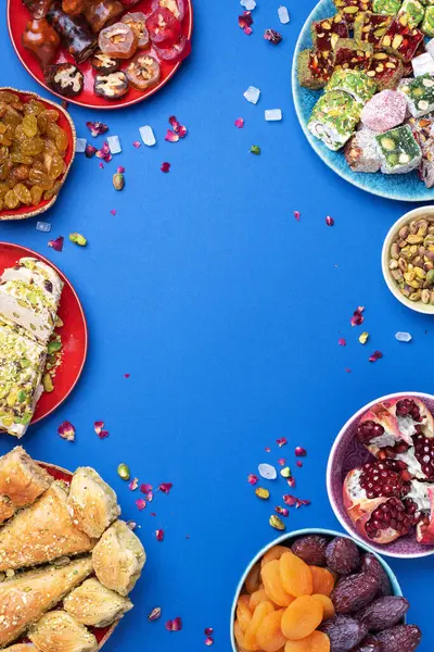 Mavi arka planda Orta Doğu tatlıları. Arap tatlısı, baklava, halva, rahat lokum, şerbet, fındık, şam fıstığı, hurma, kuru üzüm, kayısı, kilise kilisesi, kurabiye. Üst Manzara. Düz yatıyordu. Boşluğu kopyala.