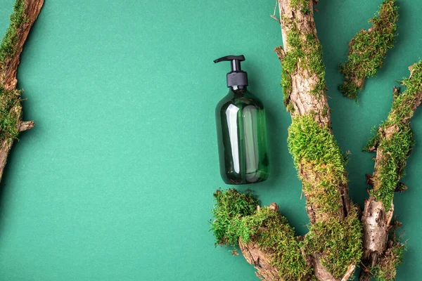 Yeşil arka planda etiketsiz kozmetik şişesi dalların üzerinde doğal yosun, ağaç kabuğu. Cilt bakımı, organik vücut bakımı, spa konsepti. Vegan çevre dostu kozmetoloji ürünü. Organik Kozmetik