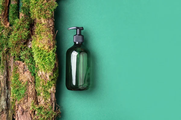 Yeşil arka planda etiketsiz kozmetik şişesi dalların üzerinde doğal yosun, ağaç kabuğu. Cilt bakımı, organik vücut bakımı, spa konsepti. Vegan çevre dostu kozmetoloji ürünü. Organik Kozmetik