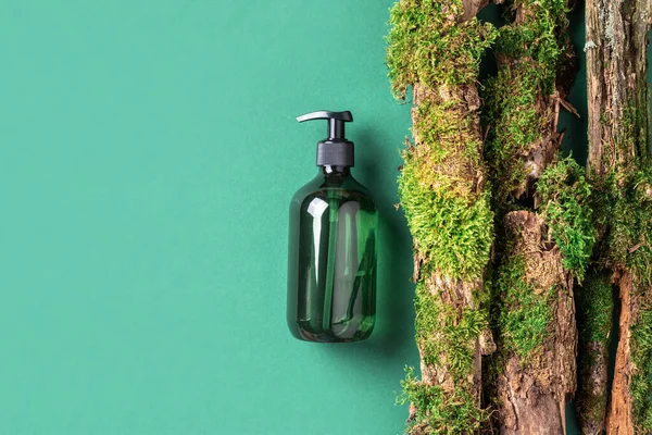 Yeşil arka planda etiketsiz kozmetik şişesi dalların üzerinde doğal yosun, ağaç kabuğu. Cilt bakımı, organik vücut bakımı, spa konsepti. Vegan çevre dostu kozmetoloji ürünü. Organik Kozmetik