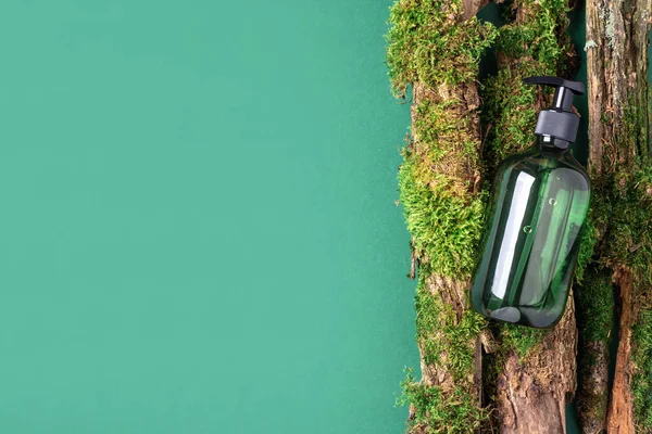 Yeşil cam şampuan, sabun, yeşil arka planda saç kremi ve ağaç kabuğunun üstünde doğal yosun. Üst görünüm, boşluğu kopyala. Model için boş etiket. Cilt bakımı, organik vücut tedavisi, spa konsepti.