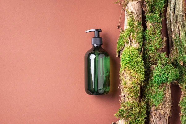 Yeşil cam şampuan, sabun, kahverengi arka planda saç kremi ve ağaç kabuğunun üstünde doğal yosun. Üst görünüm, boşluğu kopyala. Model için boş etiket. Cilt bakımı, organik vücut tedavisi, spa konsepti.