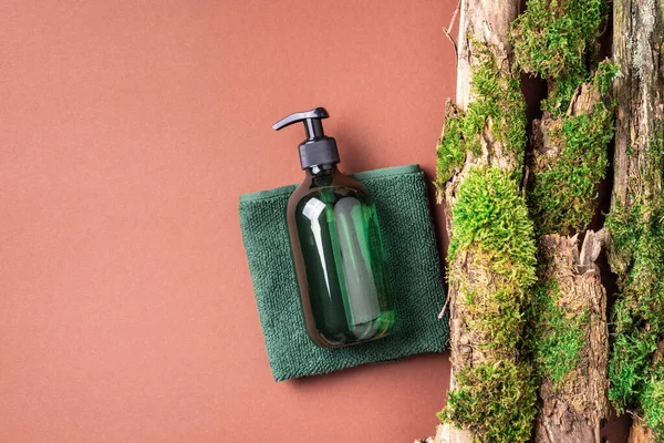 Kahverengi arka planda etiketsiz kozmetik şişesi dalların üzerinde doğal yosun, ağaç kabuğu. Cilt bakımı, organik vücut bakımı, spa konsepti. Vegan çevre dostu kozmetoloji ürünü. Organik Kozmetik