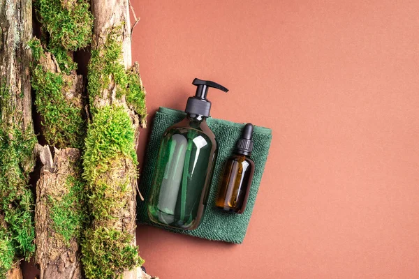 Unlabelled cosmetic bottle on brown background, natural moss over branches, bark. Skin care, organic body treatment, spa concept. Vegan eco friendly cosmetology product. Organic cosmetics