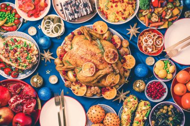 Yeni yıl yemeği masası. Kızarmış Noel tavuğu, portakal dilimleri, kızılcık, sarımsak, festival dekorasyonu, mumlar, mandalina, nar, mavi arka planda altın parıltılı yıldızlar. Üst görünüm, alanı kopyala