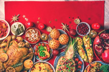 Yeni yıl yemeği masası. Kızarmış Noel tavuğu, portakal dilimleri, kızılcık, sarımsak, festival dekorasyonu, mumlar, mandalina, nar, kırmızı arka planda altın parıltılı yıldızlar. Üst görünüm, alanı kopyala