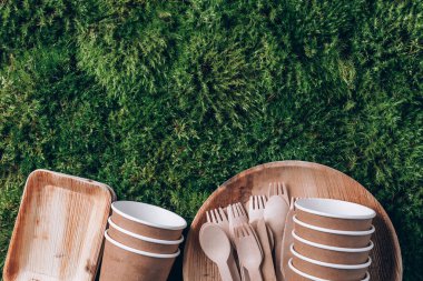 Disposable tableware from natural materials. Bamboo plates, wooden spoon, fork, knife, paper cups on green moss background. Eco-friendly sustainable lifestyle, disposable utensils. Zero waste picnic. clipart