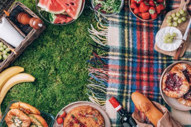 Yeşil arka planda kek, meyve, peynir, şarap ve atıştırmalıklarla yaz pikniği. Üst Manzara. Uzayı kopyala Yaz aile yemeği. Romantik piknik. Sağlıklı yiyecek ve aksesuarlarla piknik sepeti.