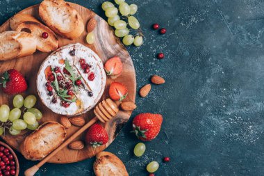 Ballı kamembert peyniri, roka, kızılcık, kızarmış ekmek, üzüm, çilek, koyu arkaplanda badem fıstığı. Üst Manzara. Uzayı kopyala Romantik randevu gecesi. Sevgililer Günü, aşk konsepti.