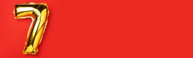 Yaratıcı düzen. Altın folyo balon numarası ve 7 haneli rakam. Doğum günü tebrik kartı. Yıldönümü konsepti. Üst Manzara. Uzayı kopyala Kırmızı zemin üzerinde zarif altın rakam. Sayısal rakam