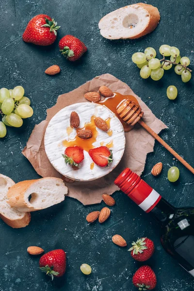 Camembert cheese with grape, almond nuts, baguette, strawberries, honey, wine on rustic dark backdrop. Top view. Copy space. Gourmet appetizer for romantic date night. Valentine\'s Day, love concept.
