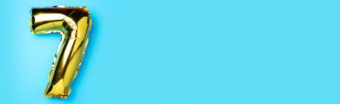 Yaratıcı düzen. Altın folyo balon numarası ve 7 haneli rakam. Doğum günü tebrik kartı. Yıldönümü konsepti. Üst Manzara. Uzayı kopyala Mavi arka planda zarif altın rakamı. Sayısal rakam