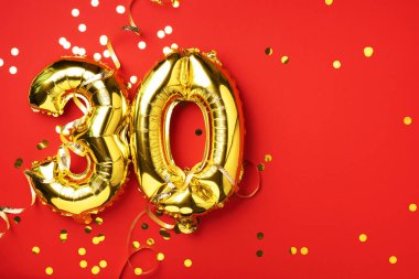 Altın folyo balon numarası, sayı 30. Doğum günü tebrik kartında 30 yazılıydı. Yıldönümü kutlaması. Pankart. Altın rakamlı, kırmızı arkaplan. Sayısal rakam, parlak parlak parıltı