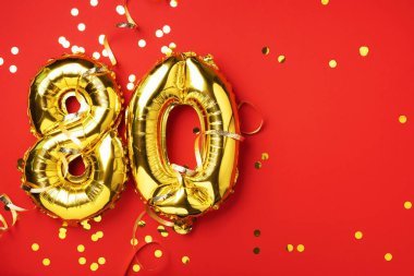 Altın folyo balon numarası, 80 haneli. 80 yazılı doğum günü tebrik kartı var. Yıldönümü kutlaması. Pankart. Altın rakamlı, kırmızı arkaplan. Sayısal rakam, parlak parlak parıltı