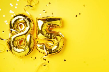 Altın folyo balon numarası, seksen beş. Doğum günü tebrik kartı, 85. yazı. Yıldönümü kutlaması. Pankart. Altın rakamlı, sarı arkaplan. Sayısal rakam, parlak parlak parıltı.