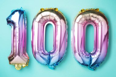 Gökkuşağı folyo balon numarası, 100 haneli rakam. Doğum günü tebrik kartında 100 yazılıydı. Yıldönümü konsepti. Üst Manzara. Mavi arka planda renkli sayı. Sayısal rakam, kutlama etkinliği
