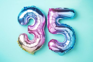 Gökkuşağı folyo balon numarası, rakam 35. Doğum günü tebrik kartında 35 yazılıydı. Yıldönümü konsepti. Üst Manzara. Mavi arka planda renkli sayı. Sayısal rakam, kutlama etkinliği.