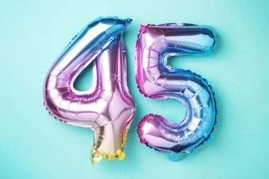 Gökkuşağı folyo balon numarası, rakam 45. 45 yazılı doğum günü tebrik kartı var. Yıldönümü konsepti. Üst Manzara. Mavi arka planda renkli sayı. Sayısal rakam, kutlama etkinliği.