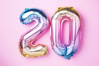 Gökkuşağı folyo balon numarası, sayı 20. Üzerinde 20 yazan doğum günü tebrik kartı. Yıldönümü konsepti. Üst Manzara. Pembe arka planda renkli sayı. Sayısal rakam, kutlama olayı, şablon.
