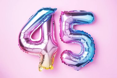 Gökkuşağı folyo balon numarası, rakam 45. 45 yazılı doğum günü tebrik kartı var. Yıldönümü konsepti. Üst Manzara. Pembe arka planda renkli sayı. Sayısal rakam, kutlama etkinliği.