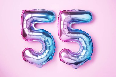 Gökkuşağı folyo balon numarası, doksan beş. 55 numaralı yazıyla birlikte doğum günü tebrik kartı. Yıldönümü konsepti. Üst Manzara. Pembe arka planda renkli sayı. Sayısal rakam, kutlama etkinliği.